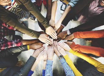 Image of people with hands extended together in a circle, representing teamwork.